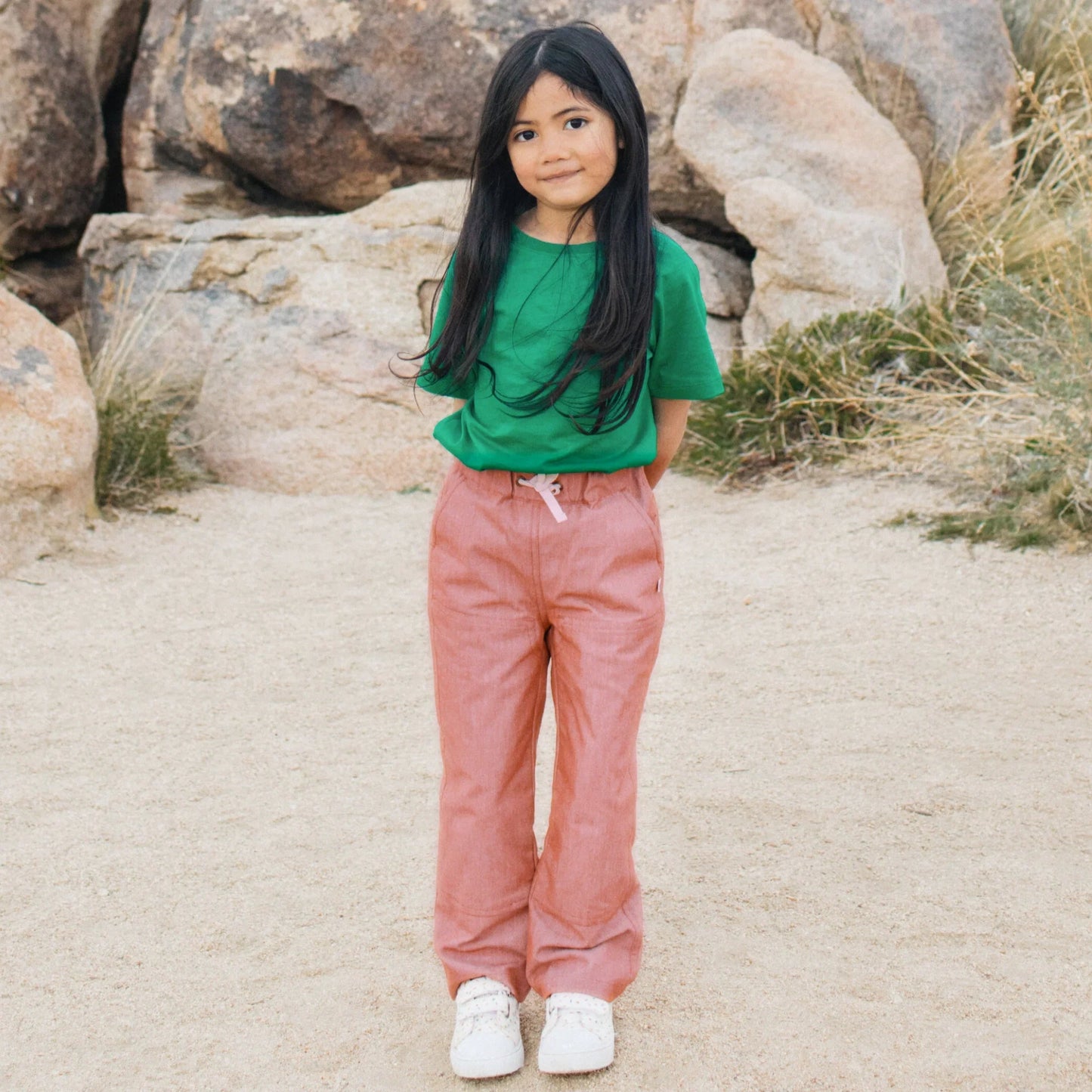 Child wearing a green shirt and pink pants standing in a rocky desert landscape
