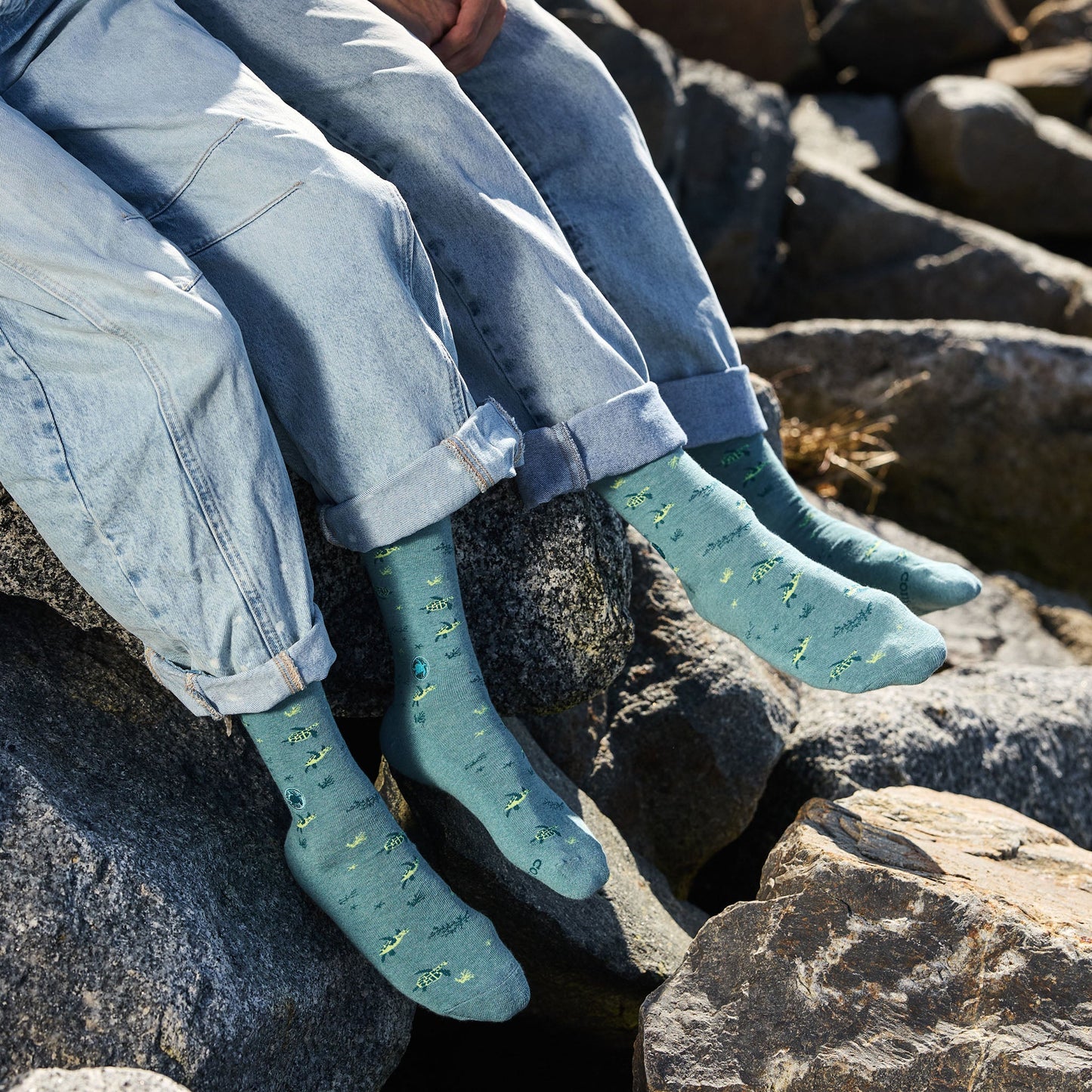 Person wearing blue jeans and green socks sitting on rocks