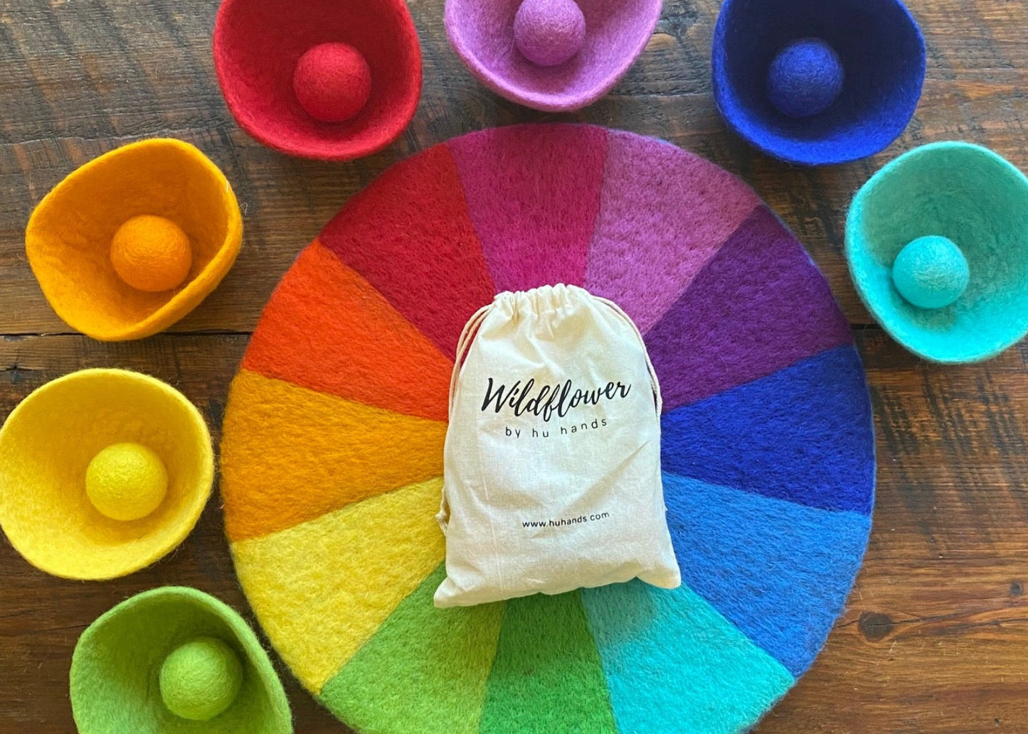 Color wheel with felt balls and a 'Wildflower' branded bag on a wooden surface