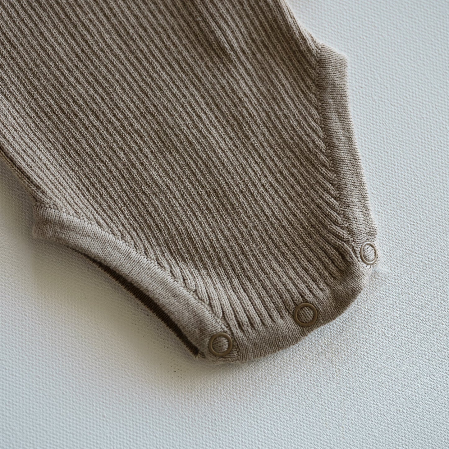 Brown ribbed baby onesie on a light gray background