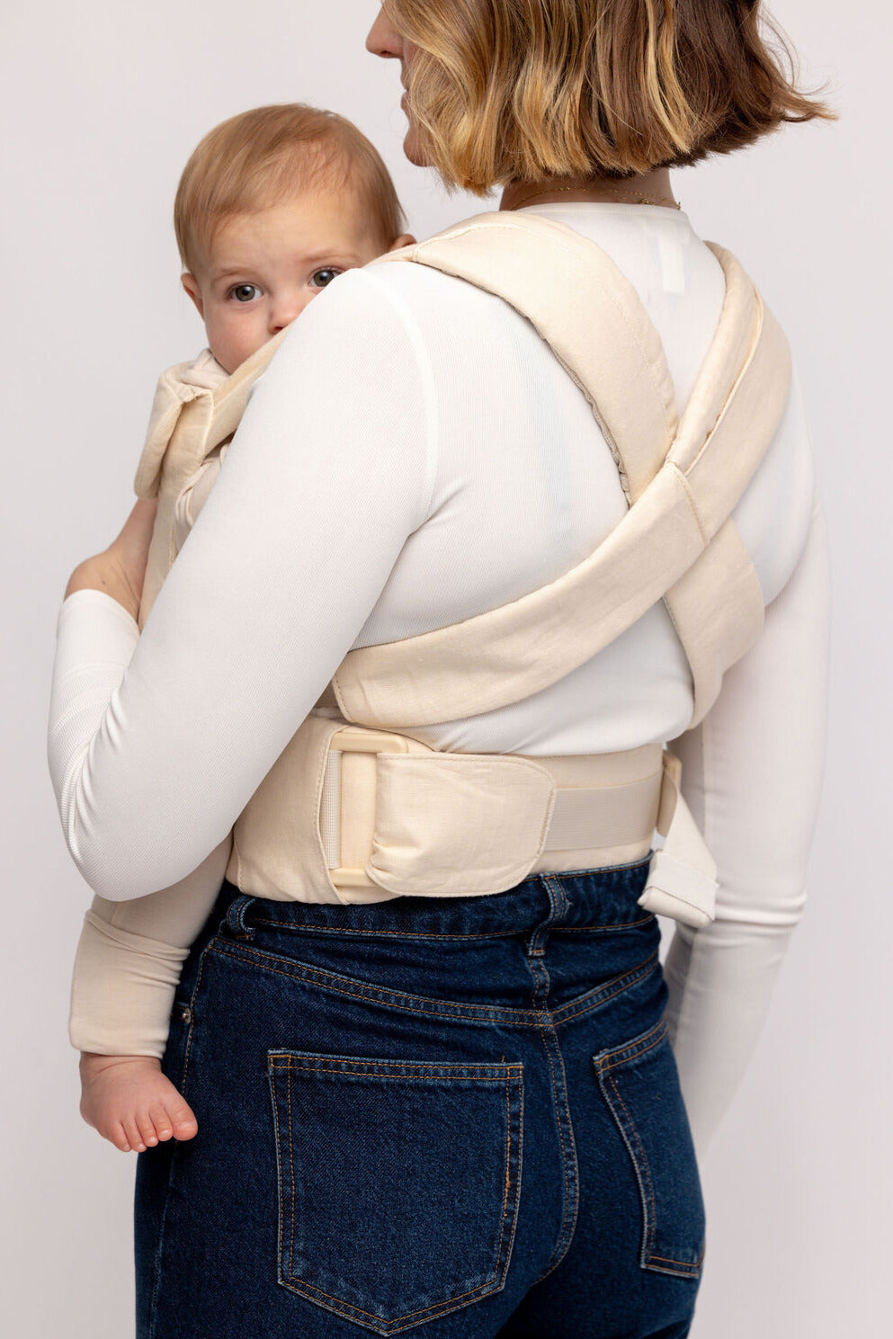 Woman wearing a baby in a beige carrier against a white background
