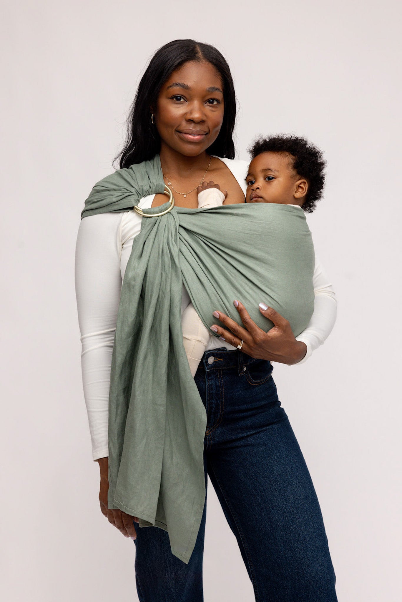 Woman holding a child in a green baby wrap against a white background