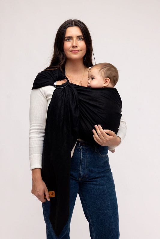 Woman holding a baby in a black wrap against a plain background