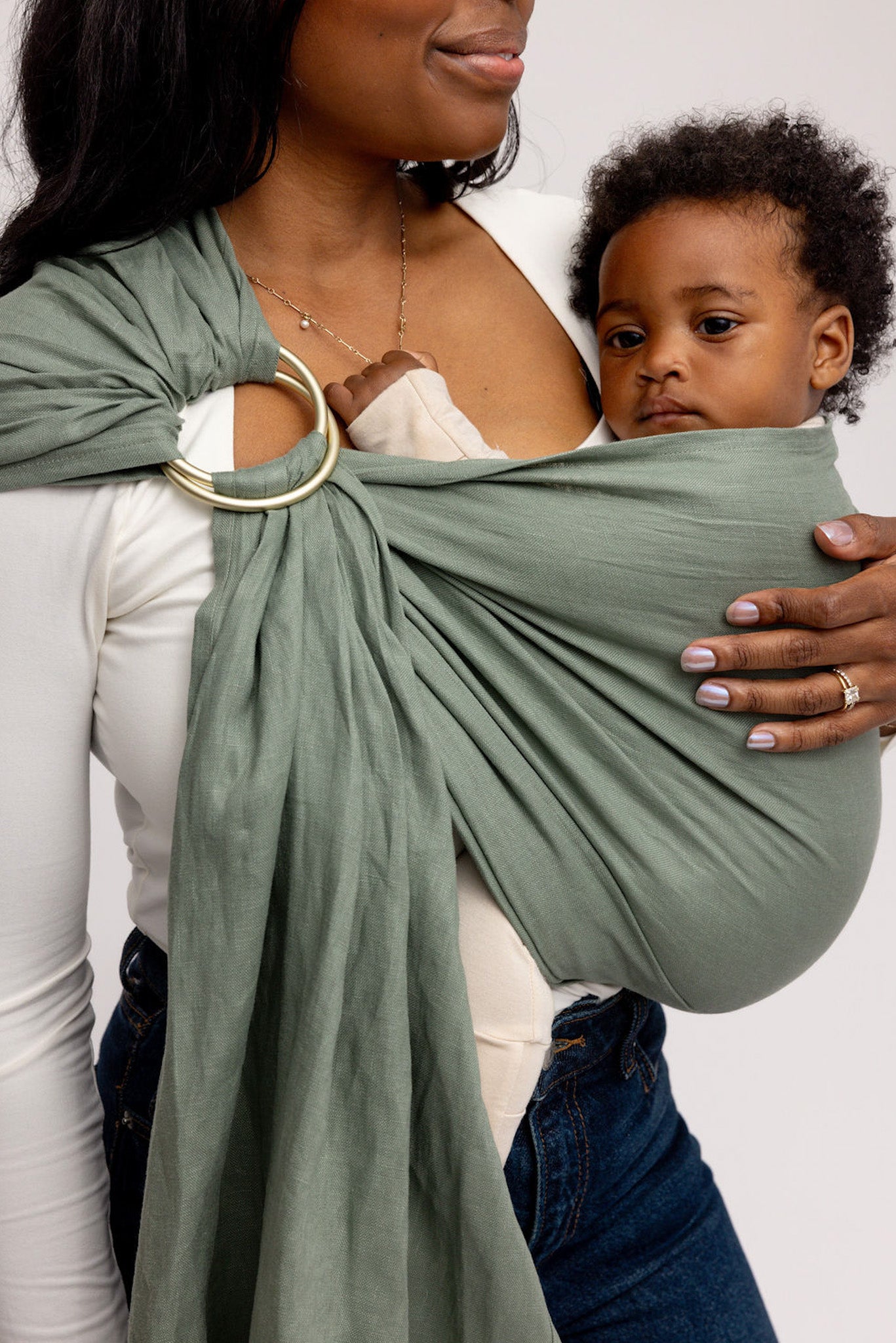Woman holding a child in a green baby wrap against a white background