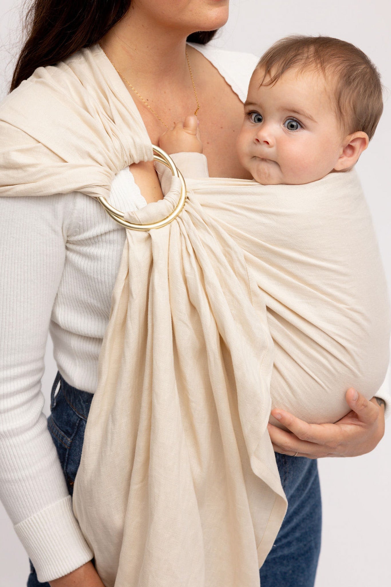 Woman holding a baby in a beige ring sling against a white background
