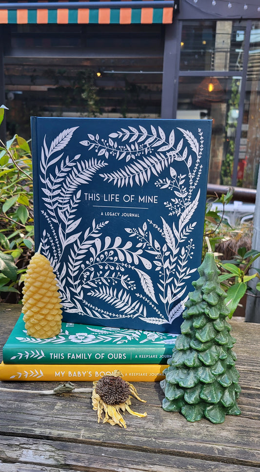 This Life of Mine stacked on two other books with flowers and candles on a. wooden table