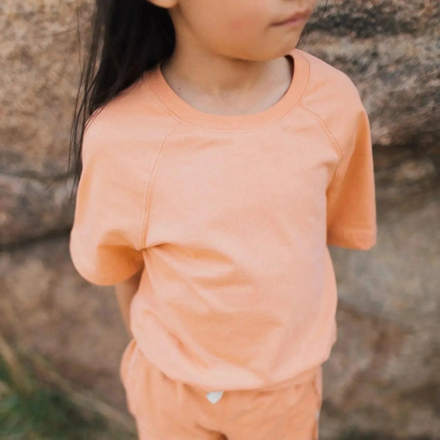 Child wearing an orange outfit standing against a stone wall.