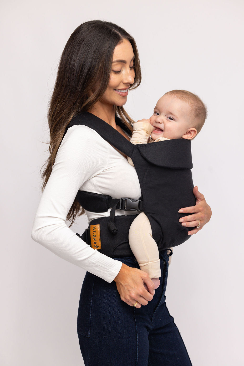 Woman holding a baby in a black baby carrier against a white background