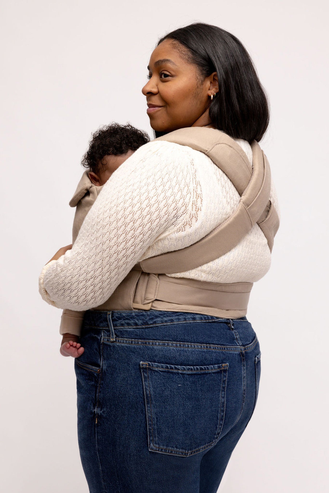Woman wearing a baby in a beige carrier against a plain background