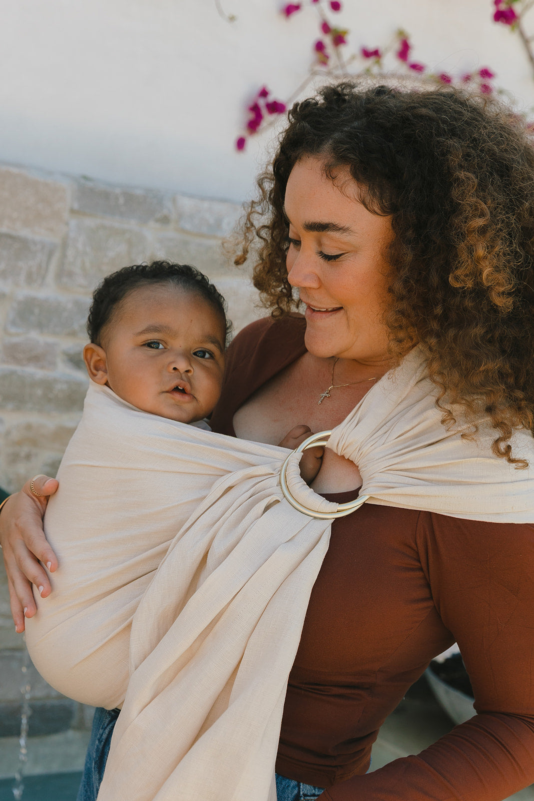 Woman holding a baby in a sling against a stone wall and floral background
