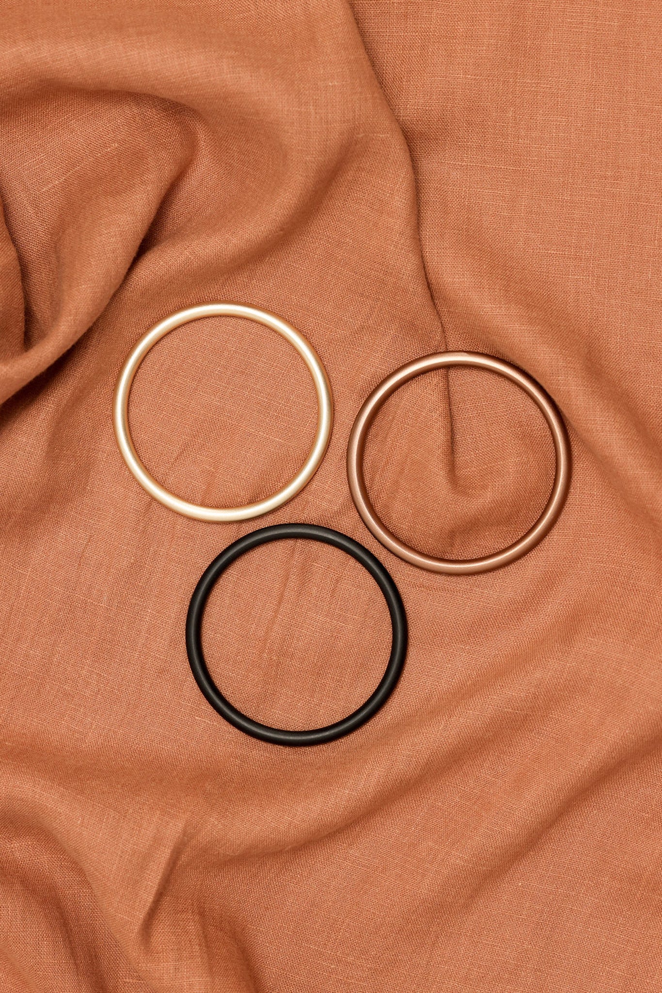 Three circular hair ties in gold, black, and bronze on a brown fabric background