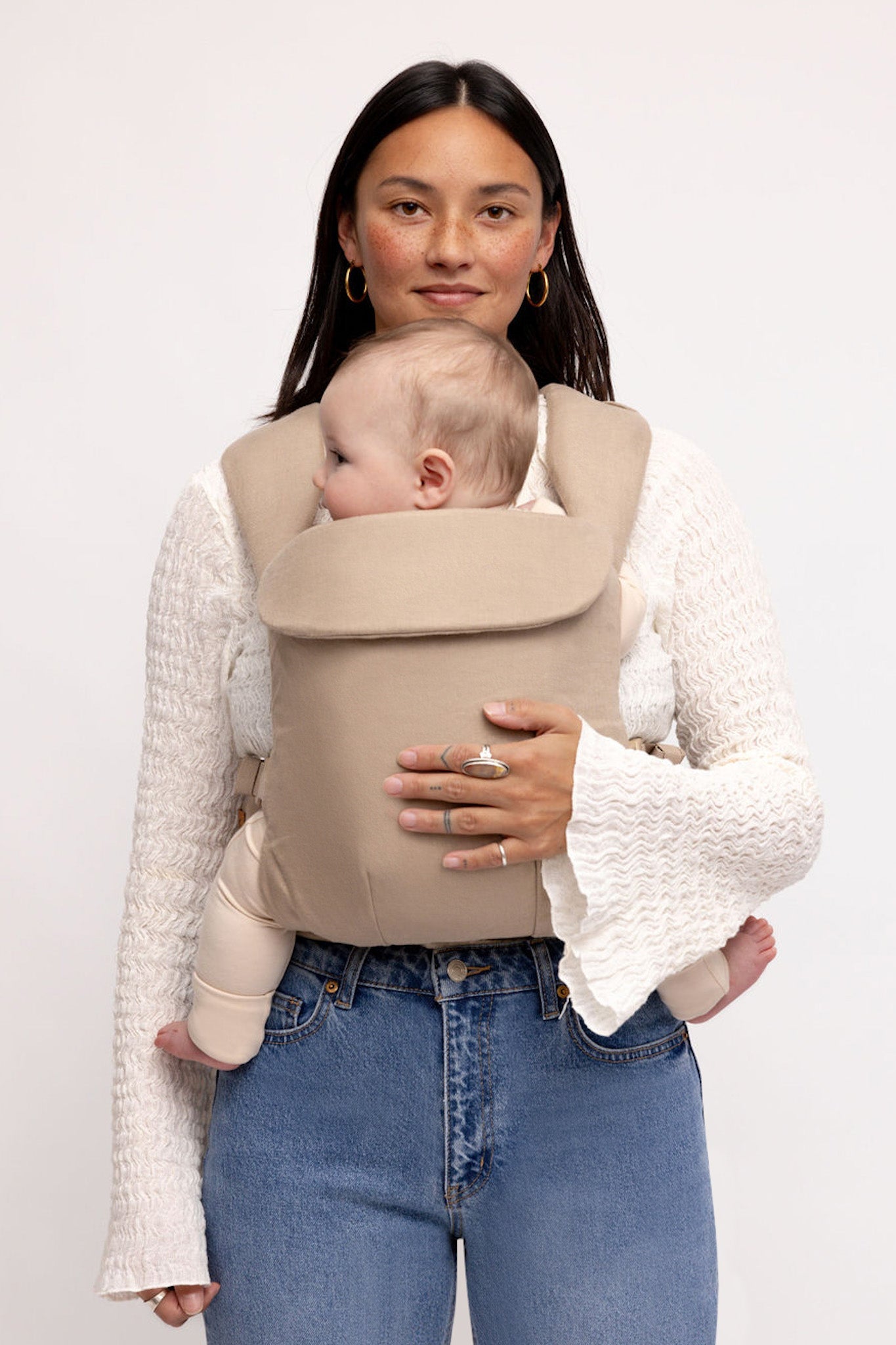 Woman holding a baby in a beige carrier against a white background