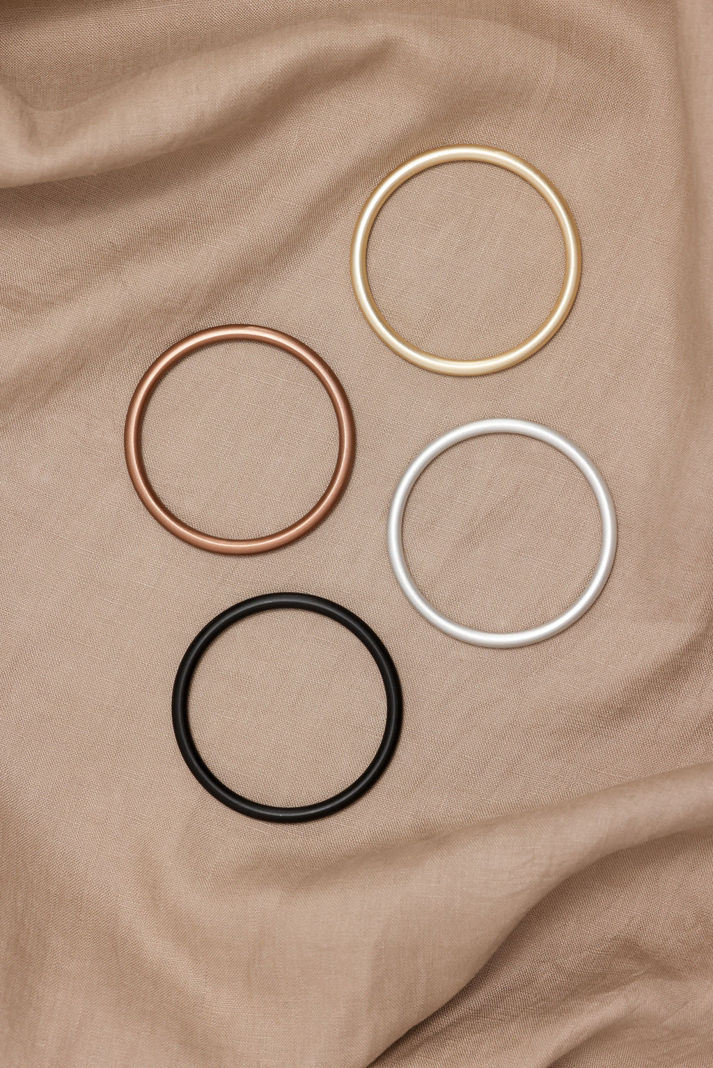 Four metallic hair ties in gold, rose gold, black, and silver on a brown fabric background.