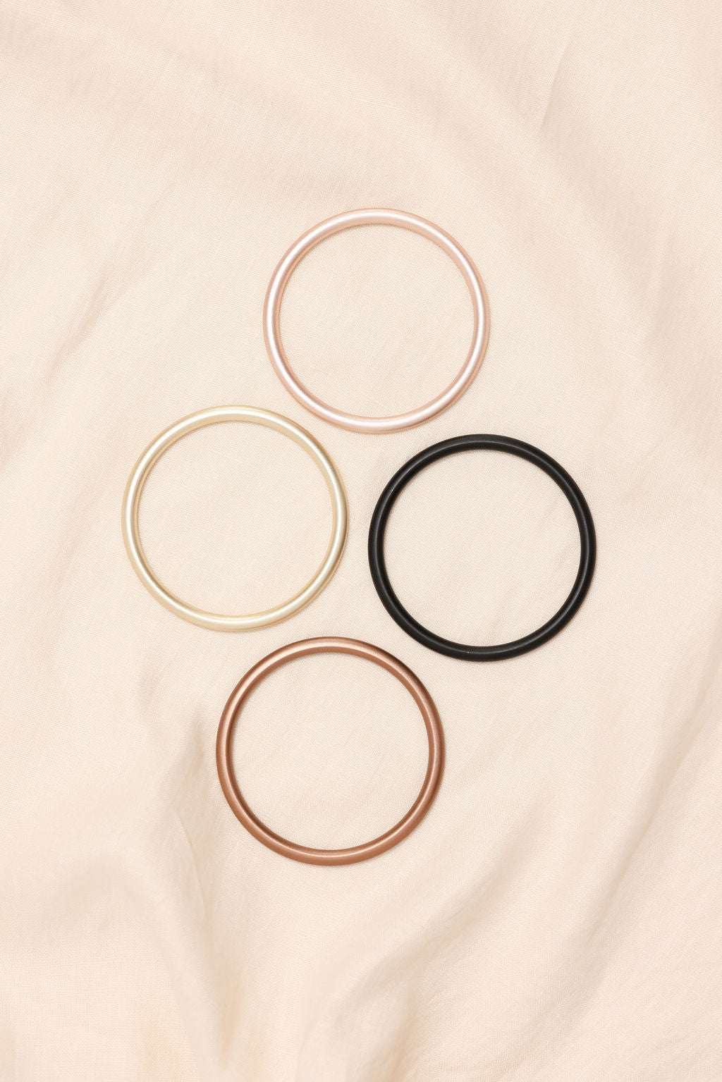 Set of five hair ties in gold, rose gold, silver, and black on a beige fabric background