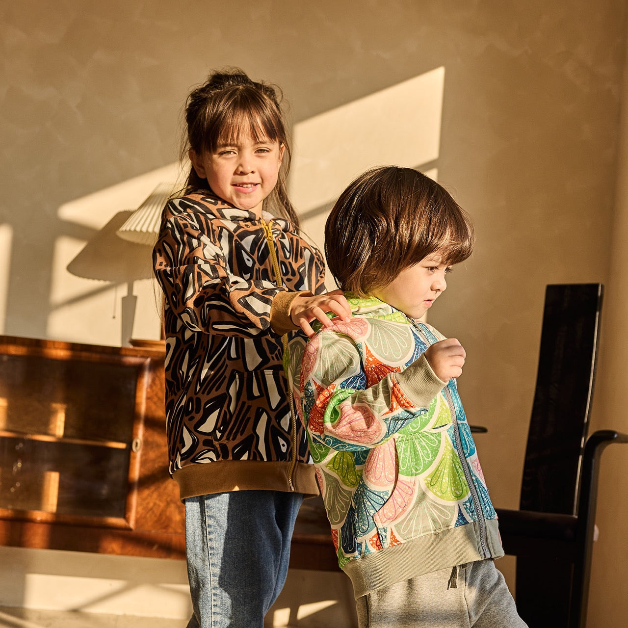 Two children standing close to each other, one wearing a patterned shirt and the other in a colorful jacket.