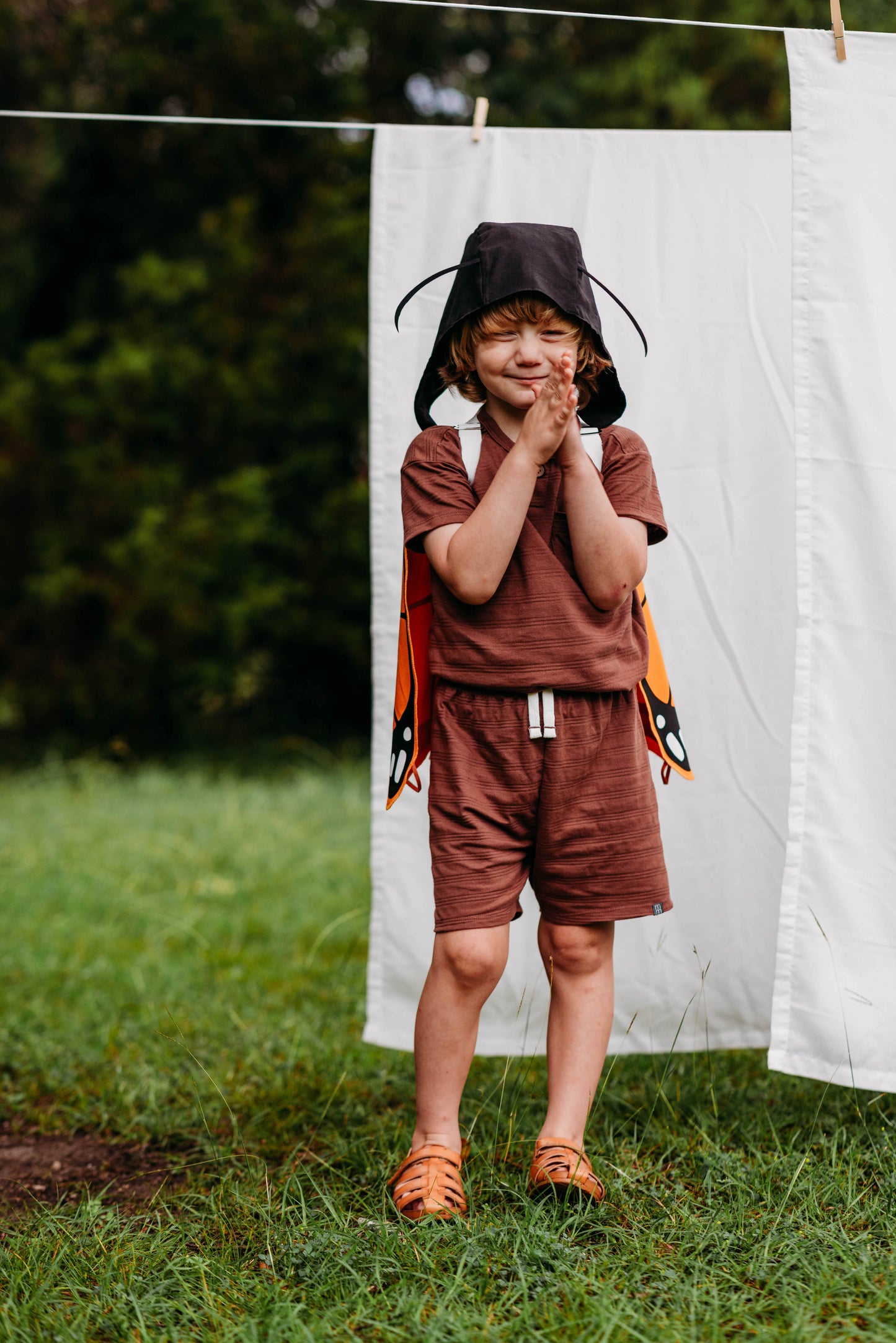 Child wearing a superhero costume standing in front of a white sheet outdoors.