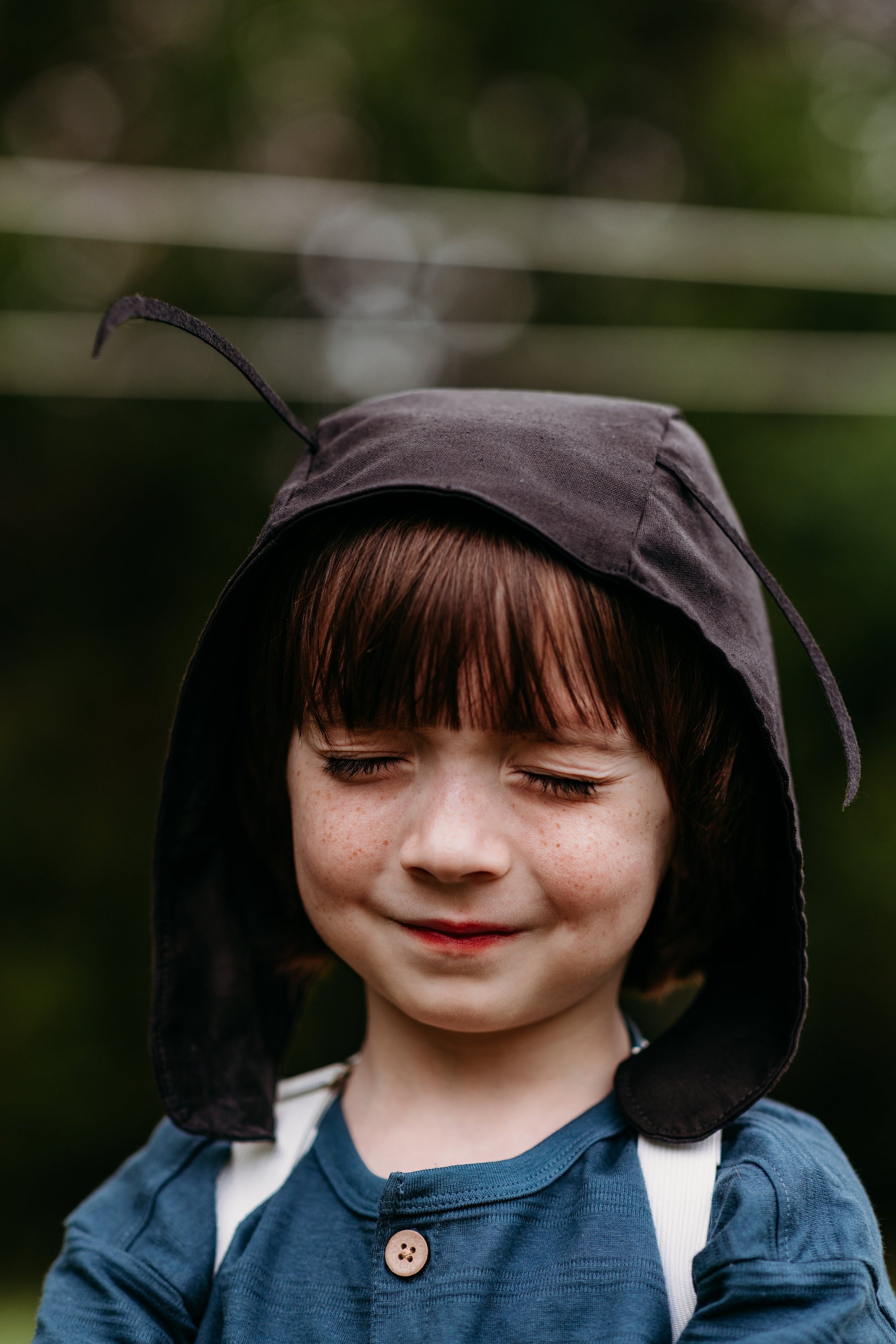 Child wearing a dark hooded garment with a blurred green background