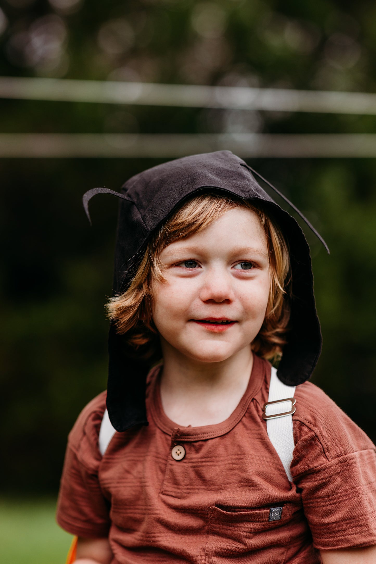 Child wearing a brown hat and outfit with a blurred green background