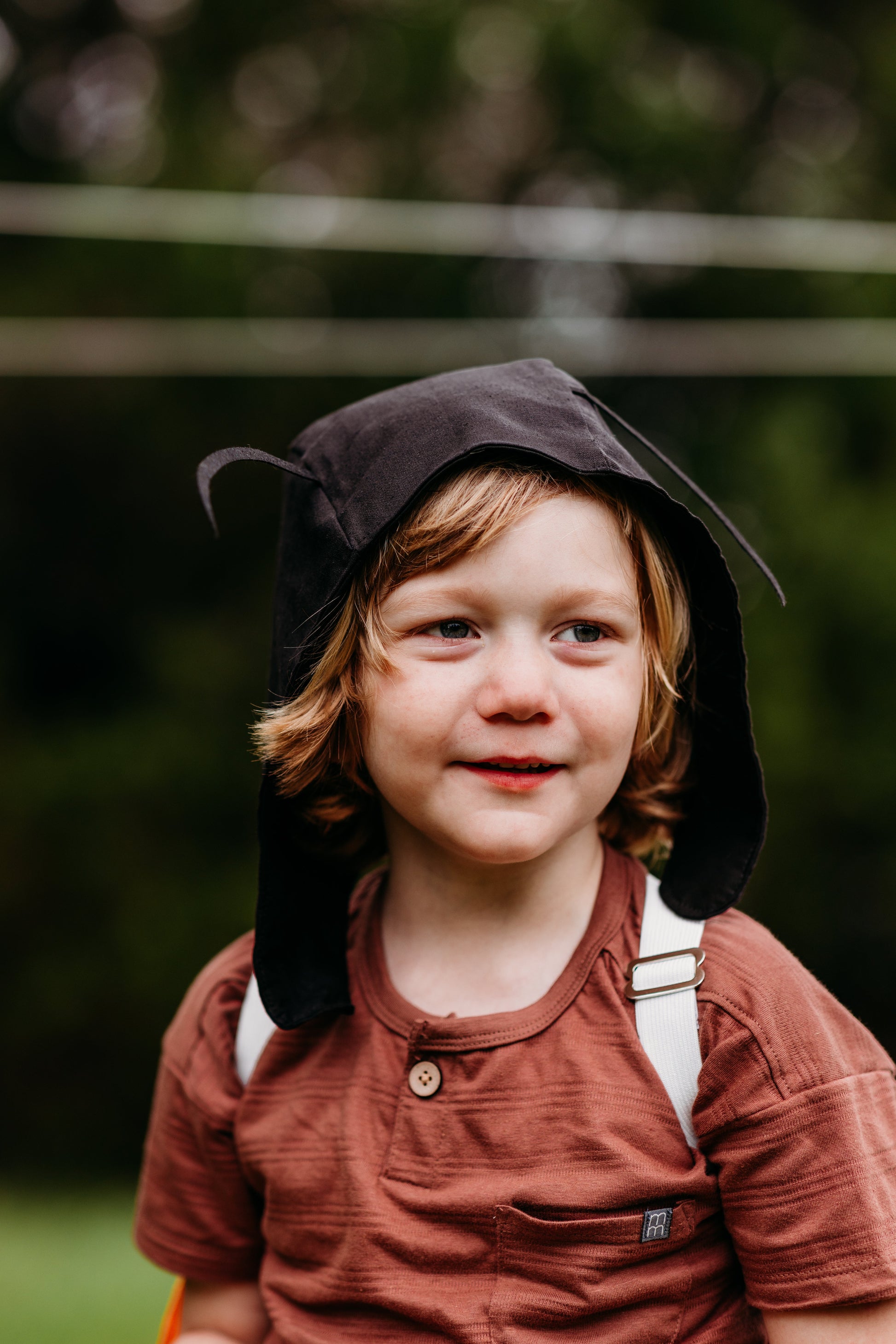 Child wearing a brown hat and outfit with a blurred green background