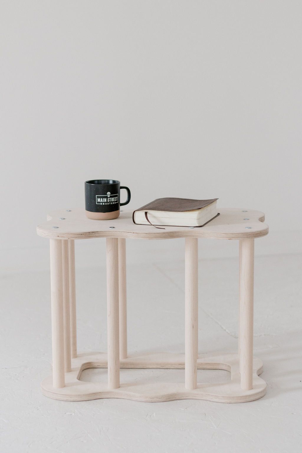 Small wooden table with a mug and book on a plain background
