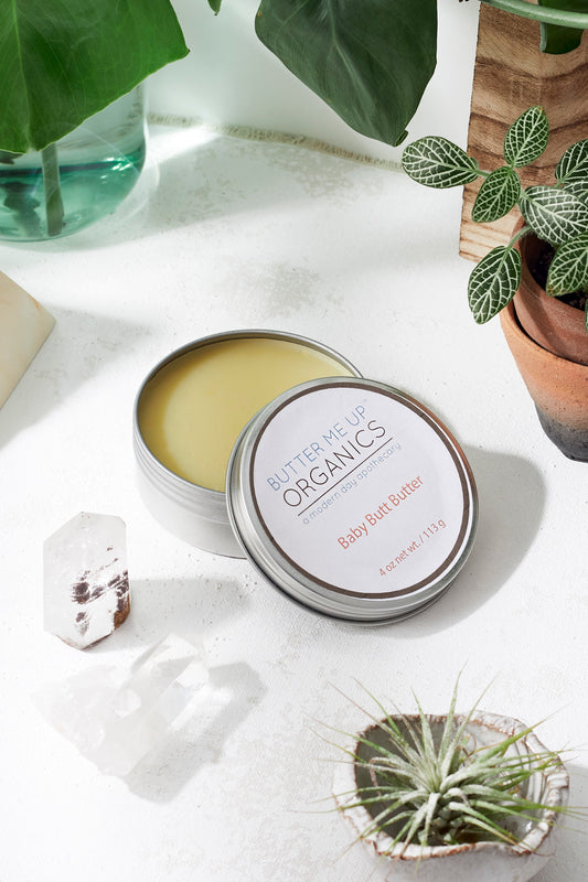 Butter Me Up Organics baby foot butter tin on a white surface with plants in the background