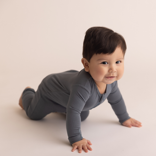 Baby in a gray outfit crawling on a plain background
