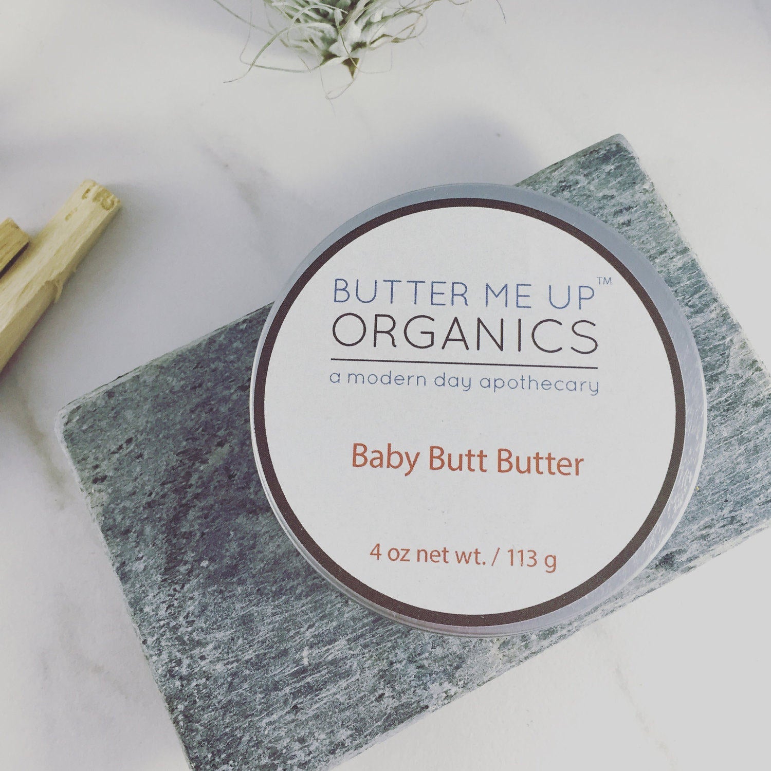 Butter Me Up Organics Baby Butt Butter container on a textured surface