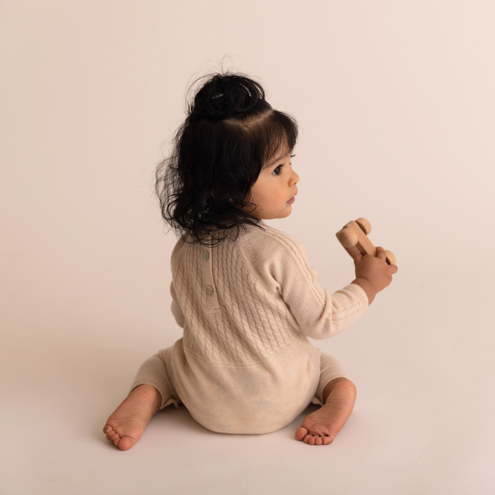 Child in a beige knitted outfit sitting on a plain background