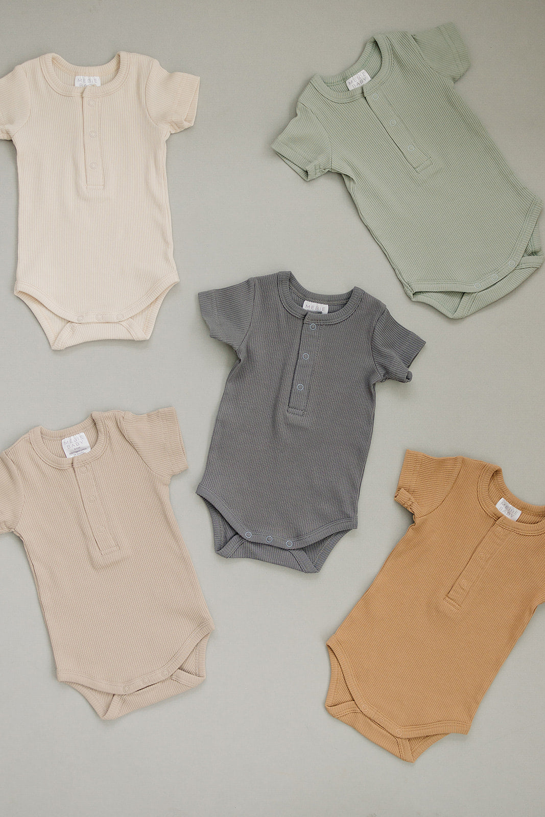 Five baby rompers in beige, green, and brown on a gray background