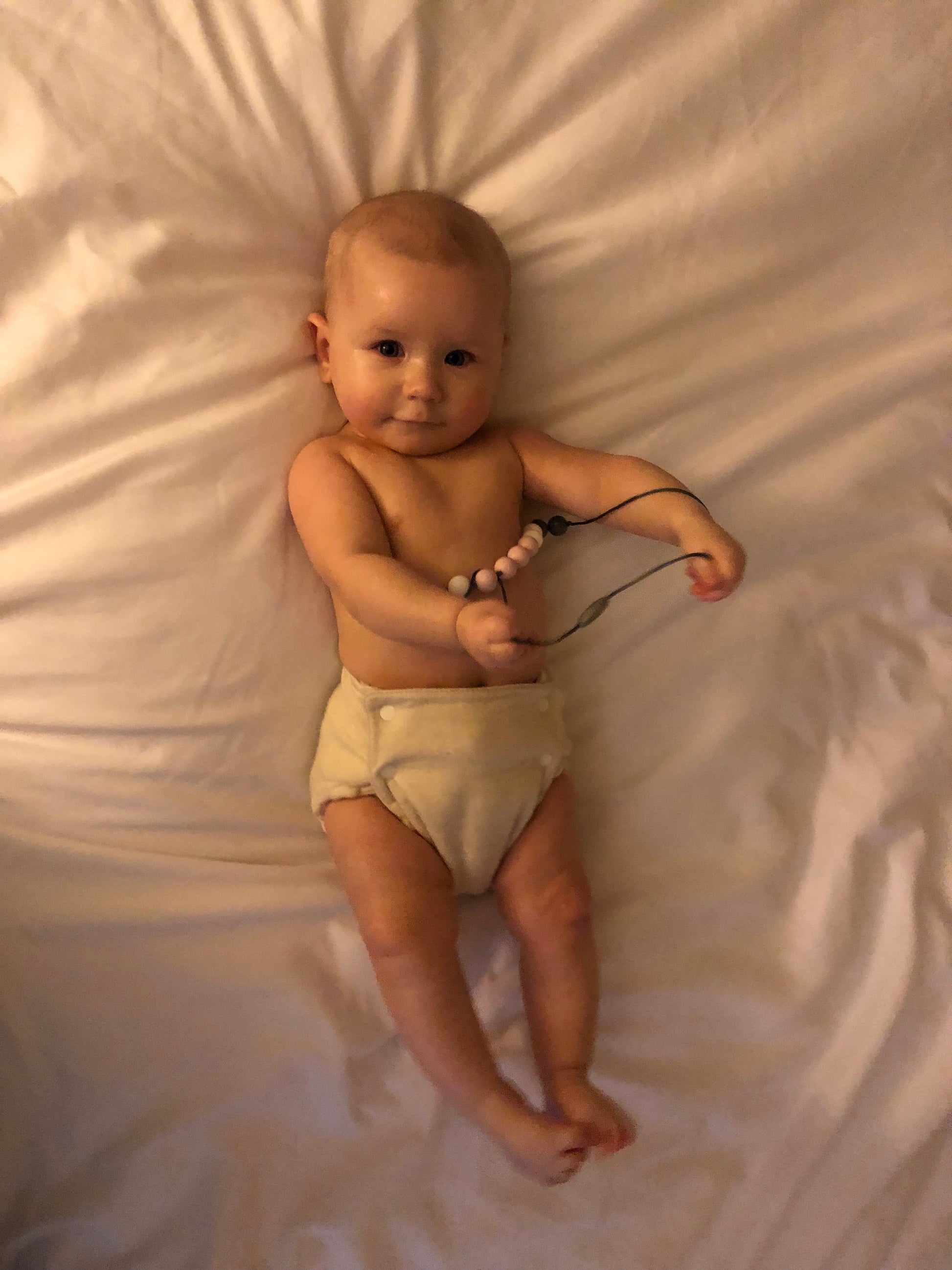 Baby lying on a white blanket holding a black cord