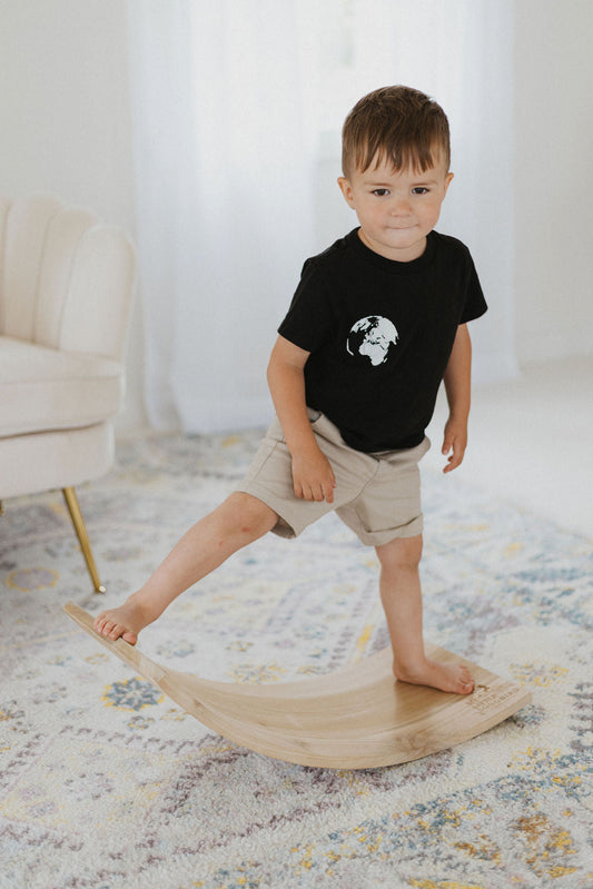 Child standing on a wooden balance board in a home setting