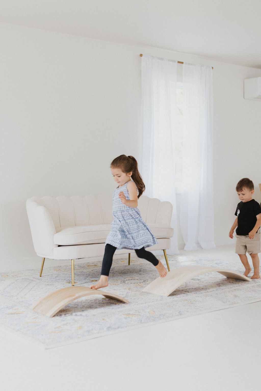 Two children playing on a wooden balance beam in a minimalistic room.