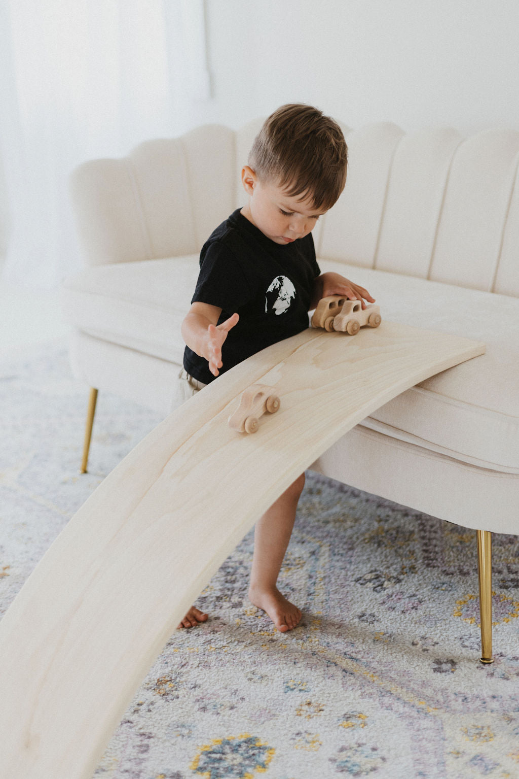 Child playing with a wooden surfboard in a living room.