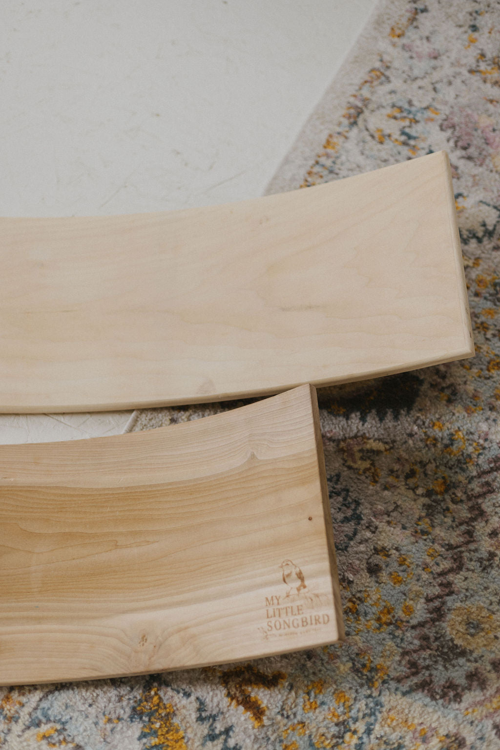 Two wooden boards on a textured rug with a brand logo.