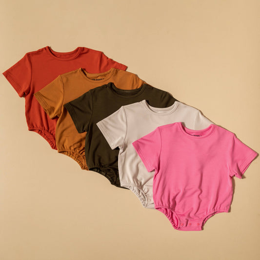 Five colorful baby rompers arranged on a beige background