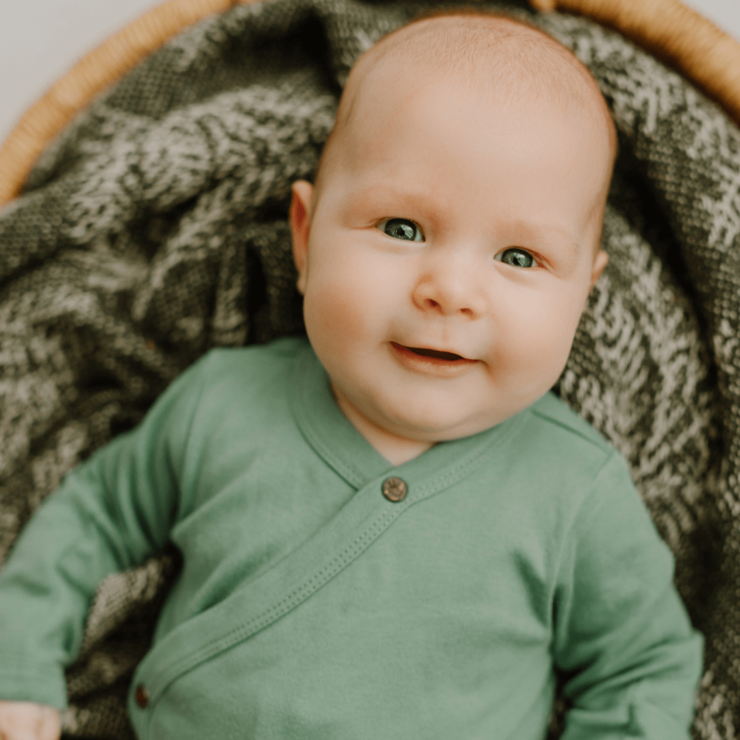 Baby wearing a green onesie sitting on a textured surface