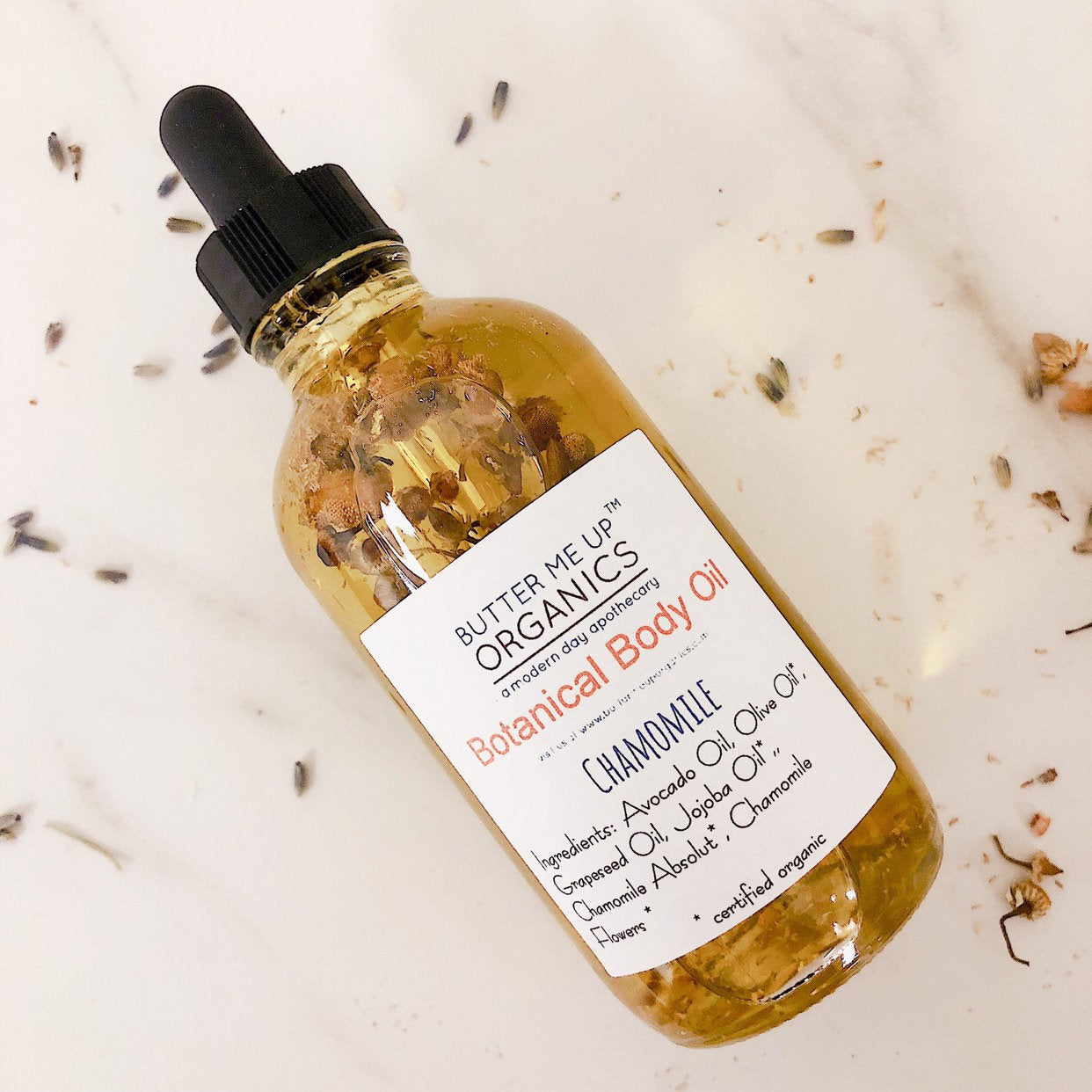 Bottle of Butter Me Up Organics botanical body oil with a dropper on a light background.