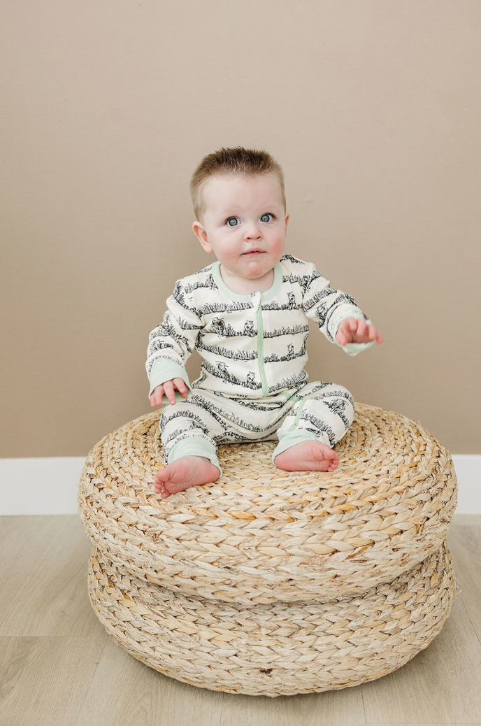 Baby sitting on a woven ottoman against a beige wall