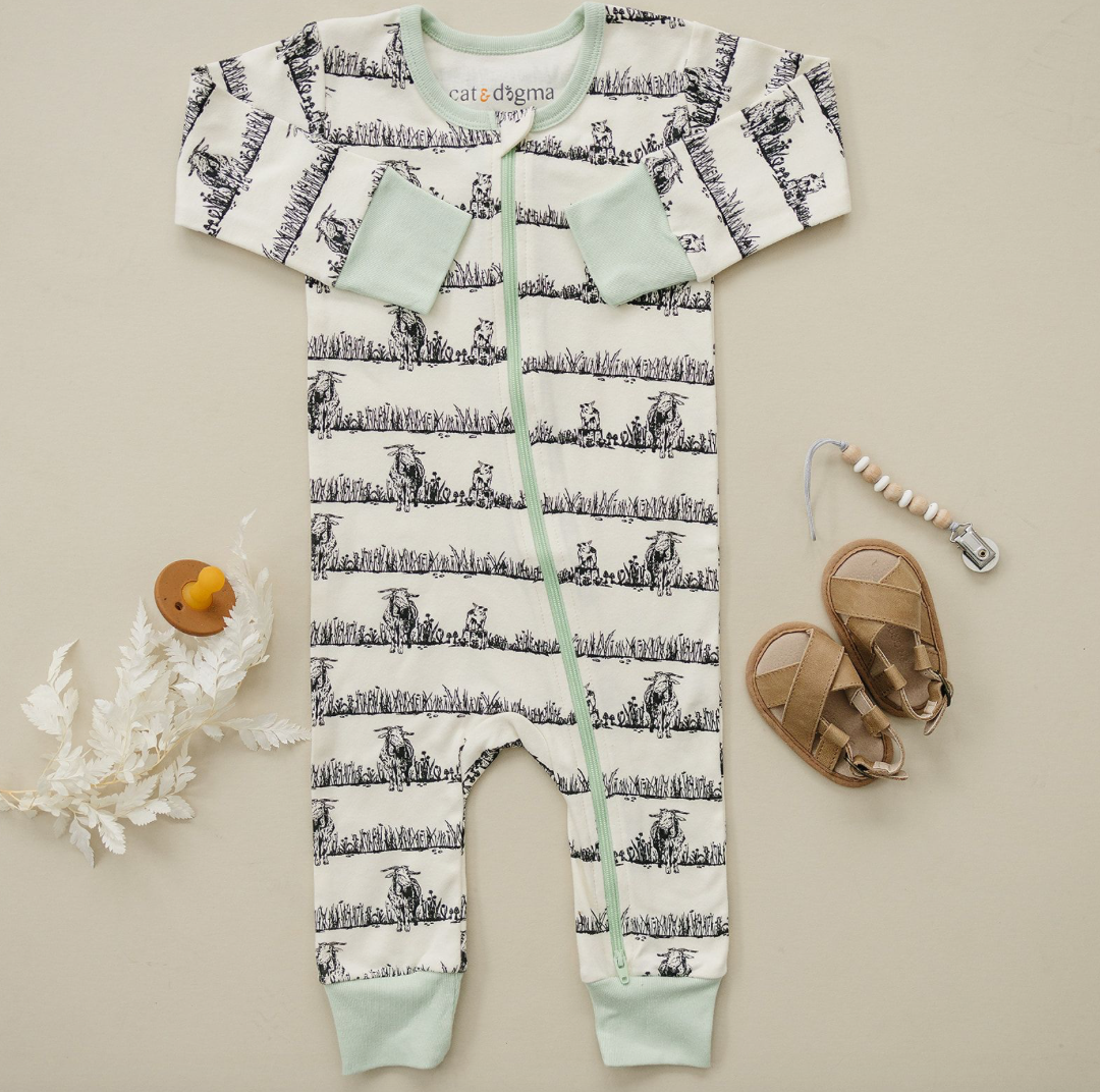 Baby onesie with cow print and mint accents on a beige background
