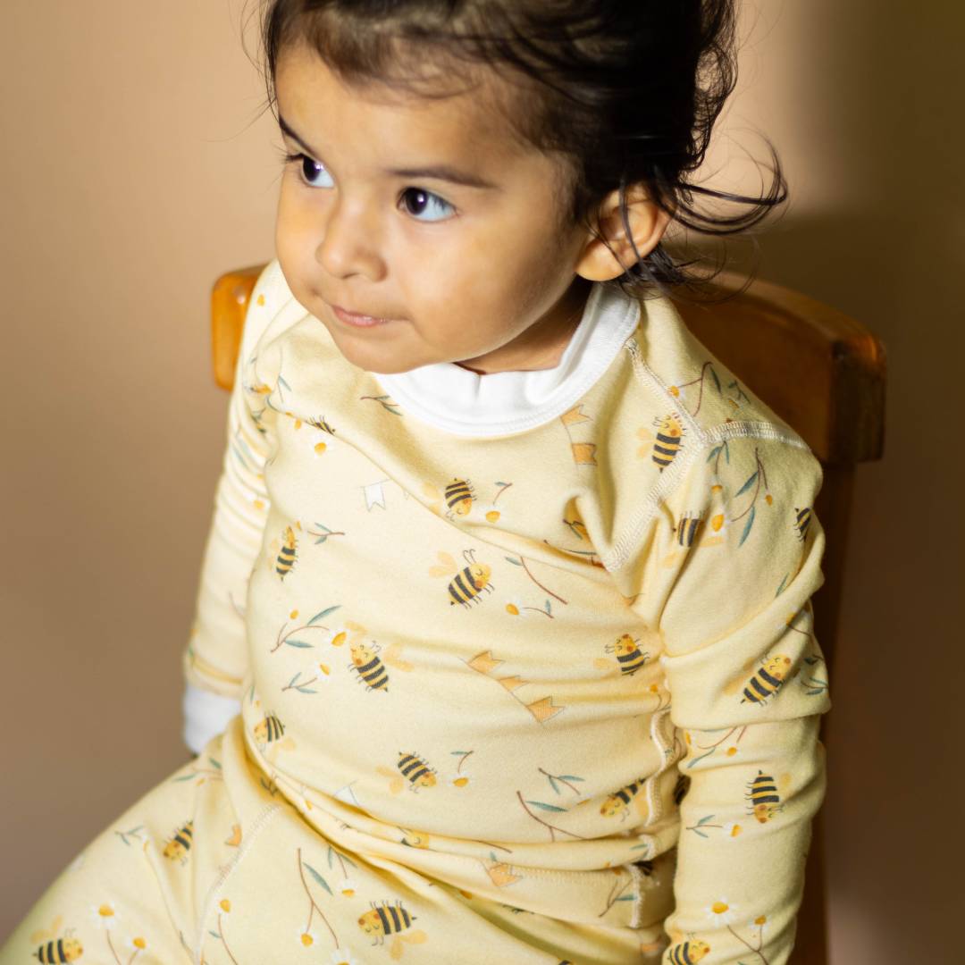 Child wearing a yellow dress with bee pattern sitting on a chair.