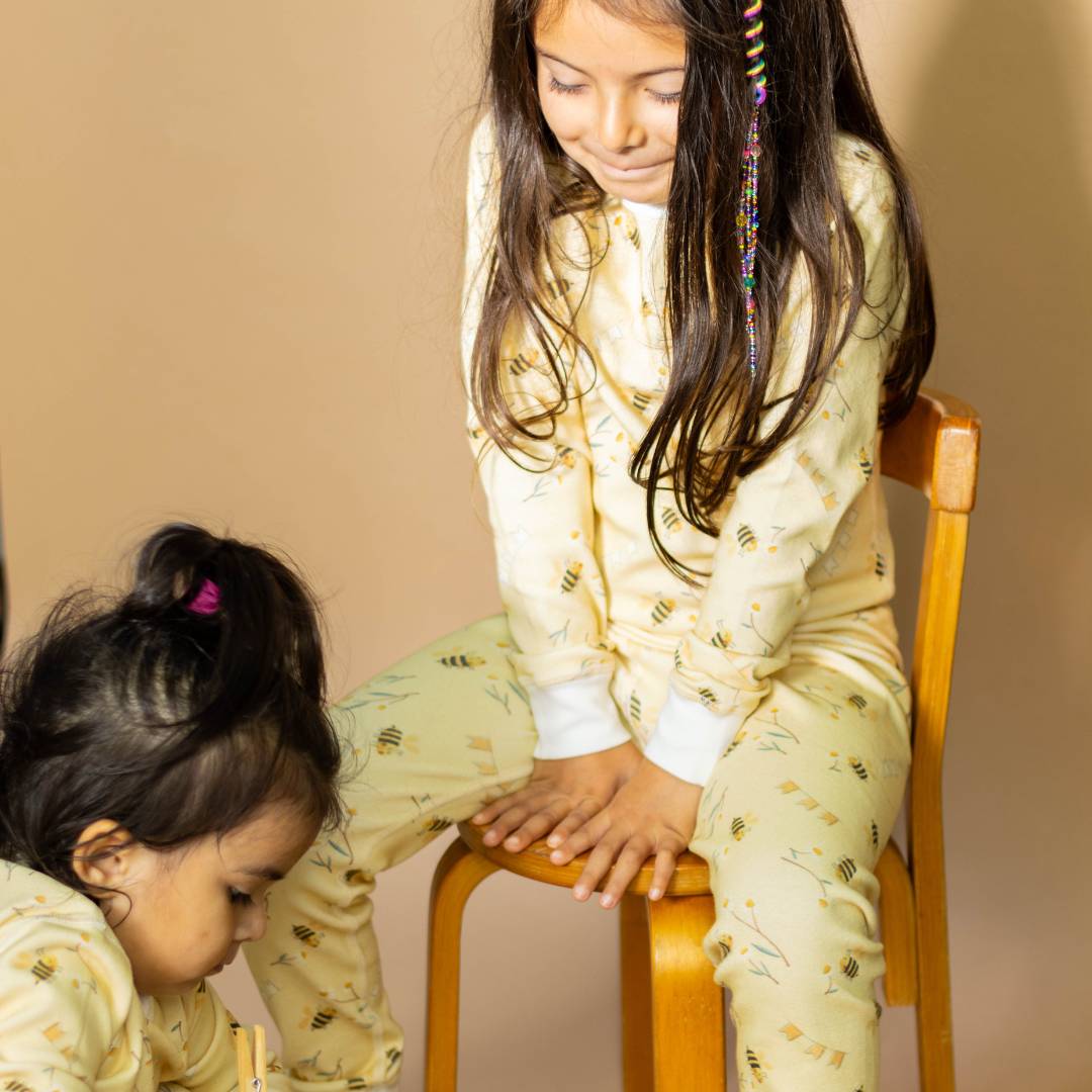 Two children in matching pajamas sitting on a chair against a beige background