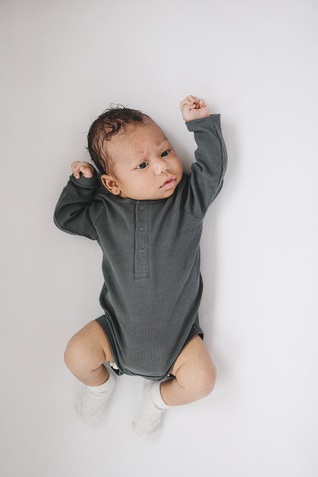 Baby wearing a gray long-sleeve onesie on a plain background