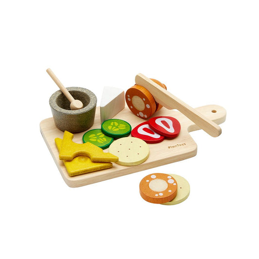 Wooden toy food set with cutting board, vegetables, and a mortar and pestle on a white background
