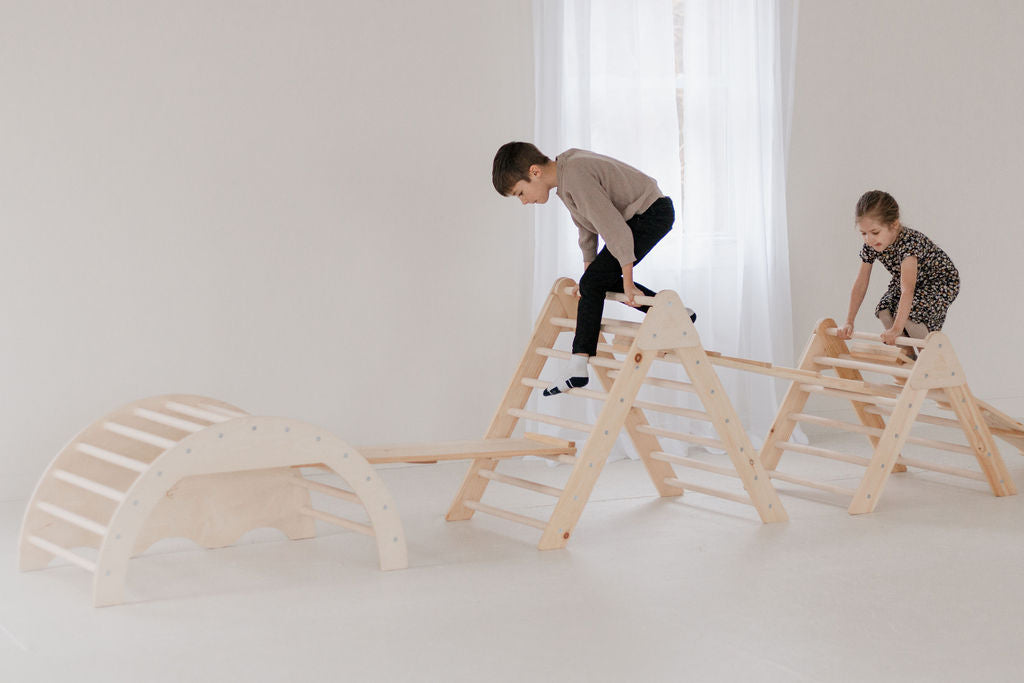 Children playing on wooden climbing structures in a minimalistic room.
