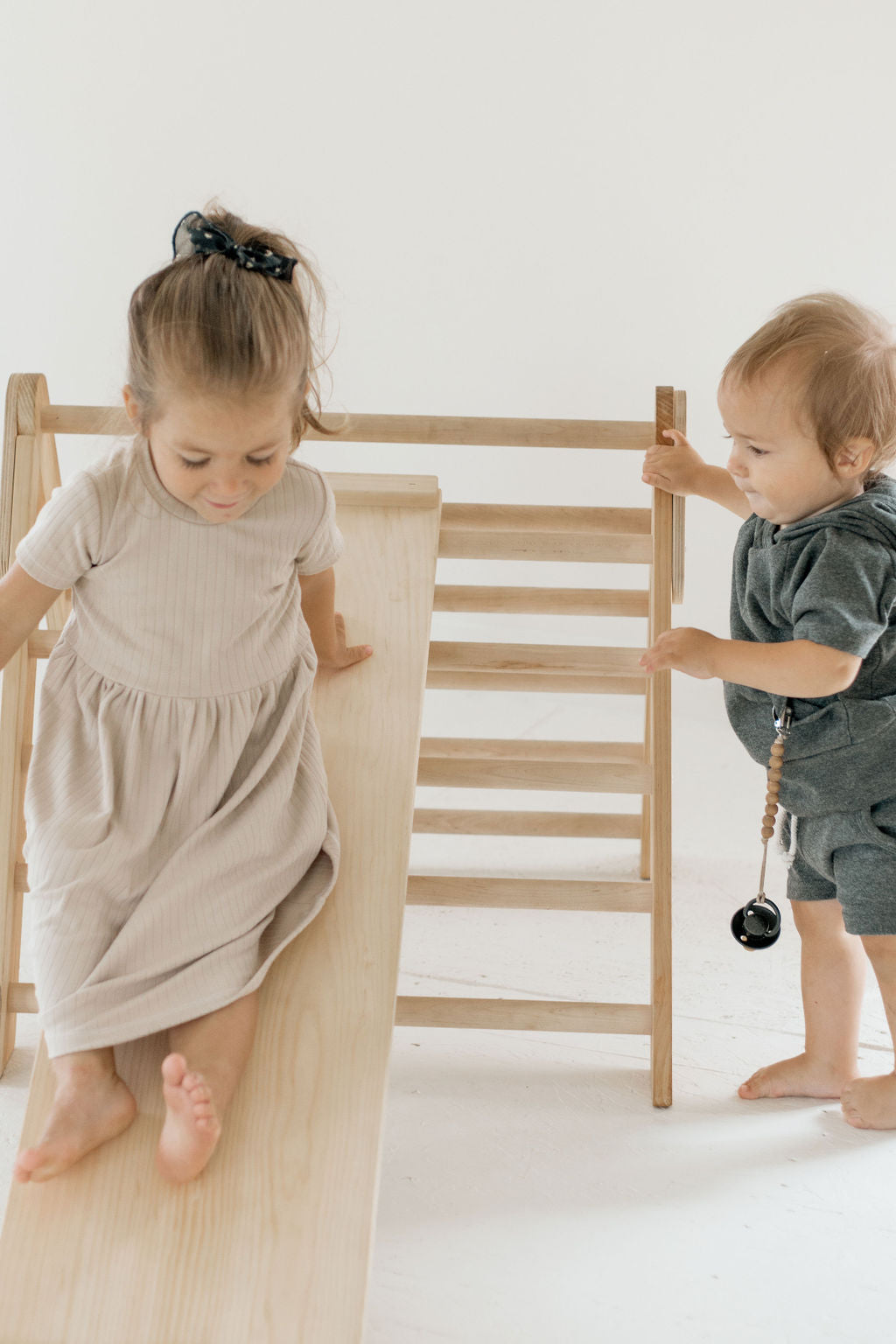 Two children playing on a wooden climbing toy against a white background