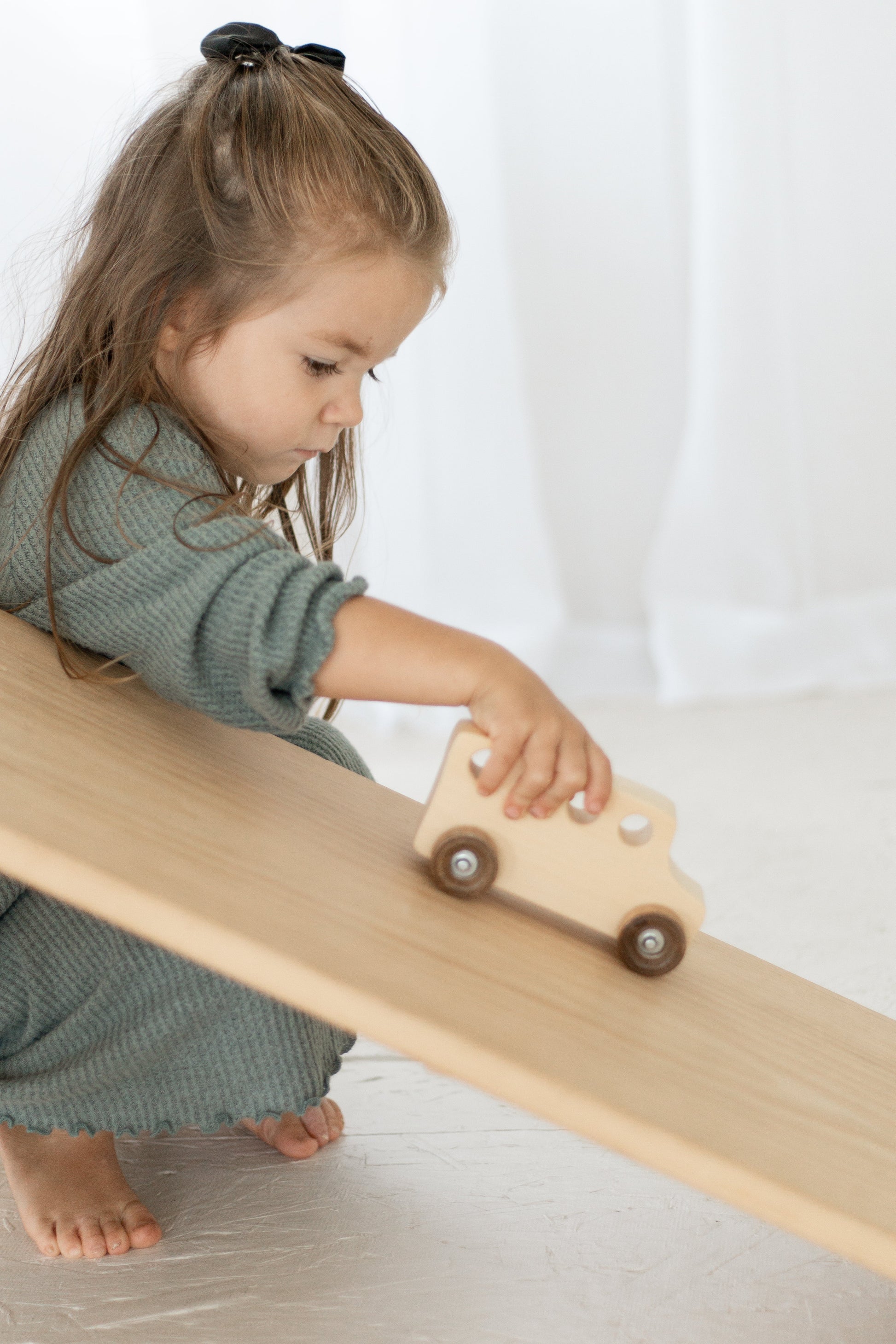 Child playing with a wooden toy car on a ramp indoors