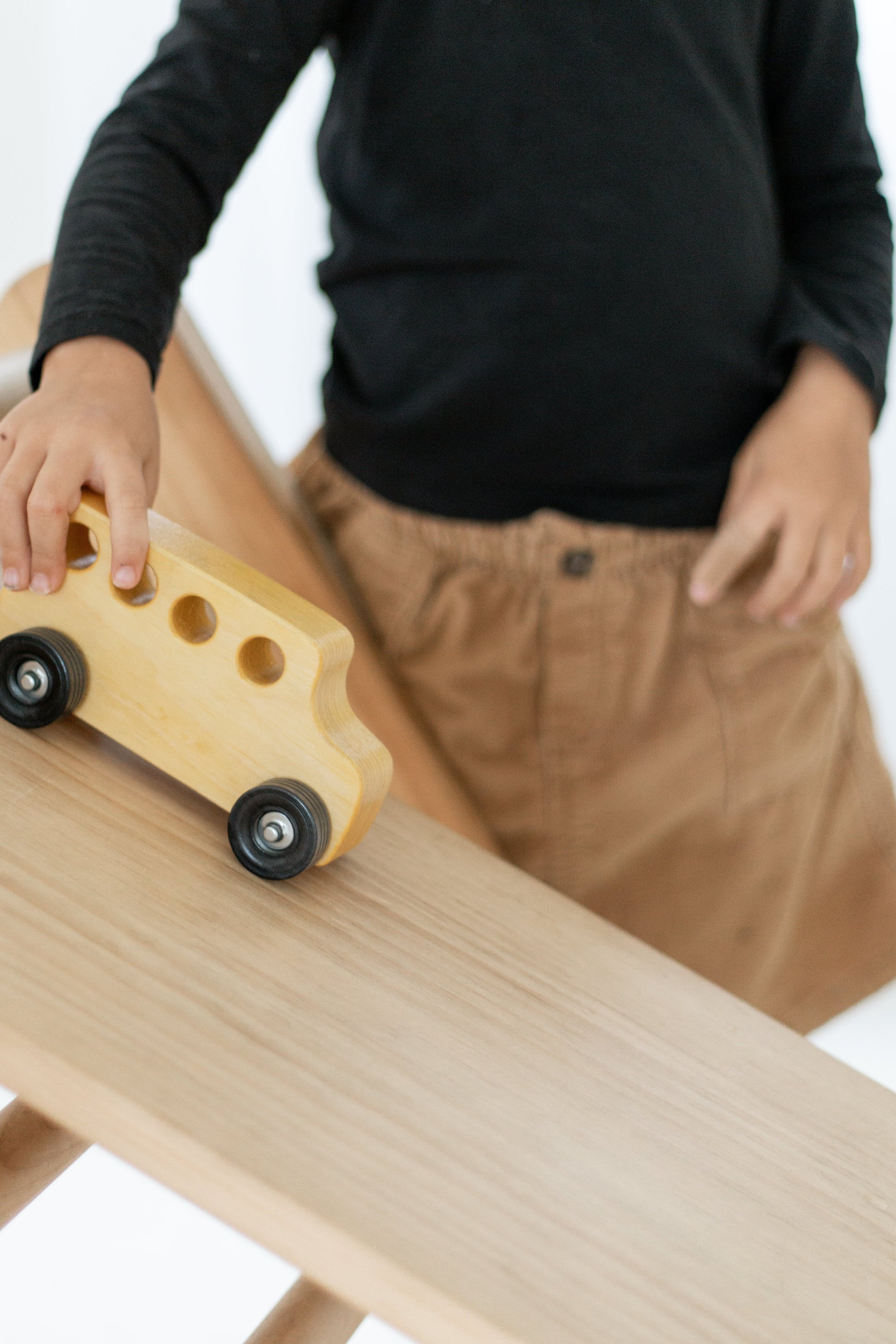 Child playing with a wooden toy car on a ramp