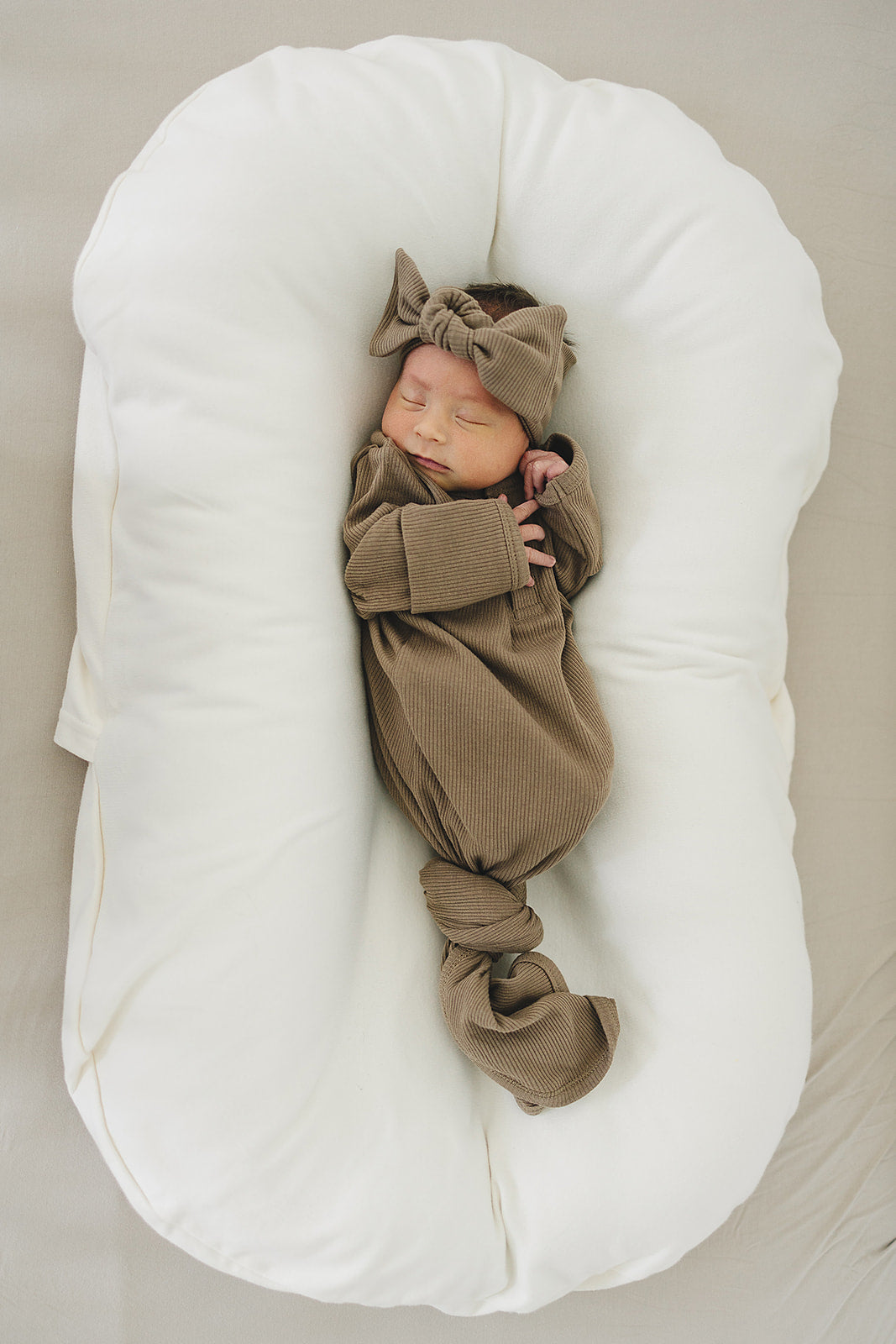 Newborn baby wrapped in a brown outfit lying on a white cushion