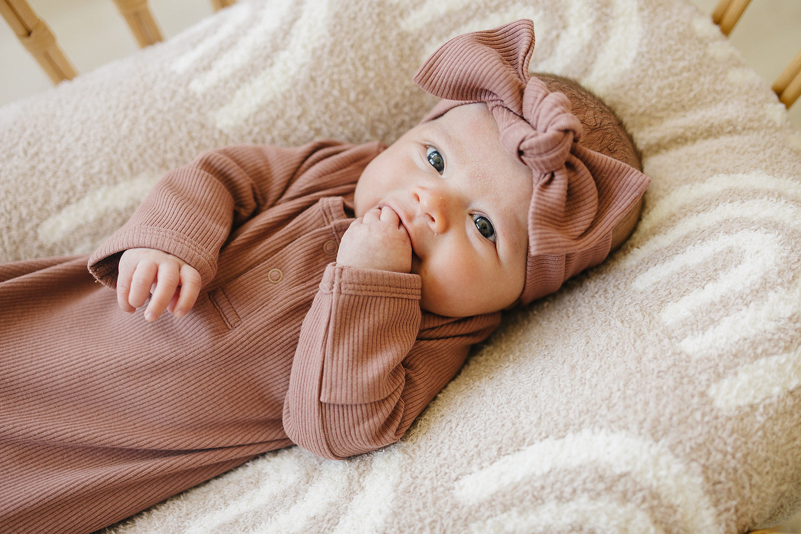 Baby in a pink outfit with a large bow lying on a soft blanket
