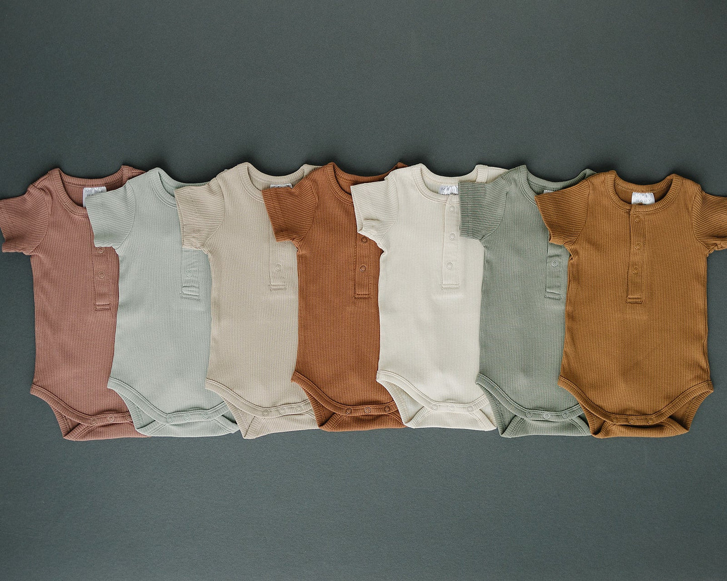 Row of baby bodysuits in various colors on a dark gray background